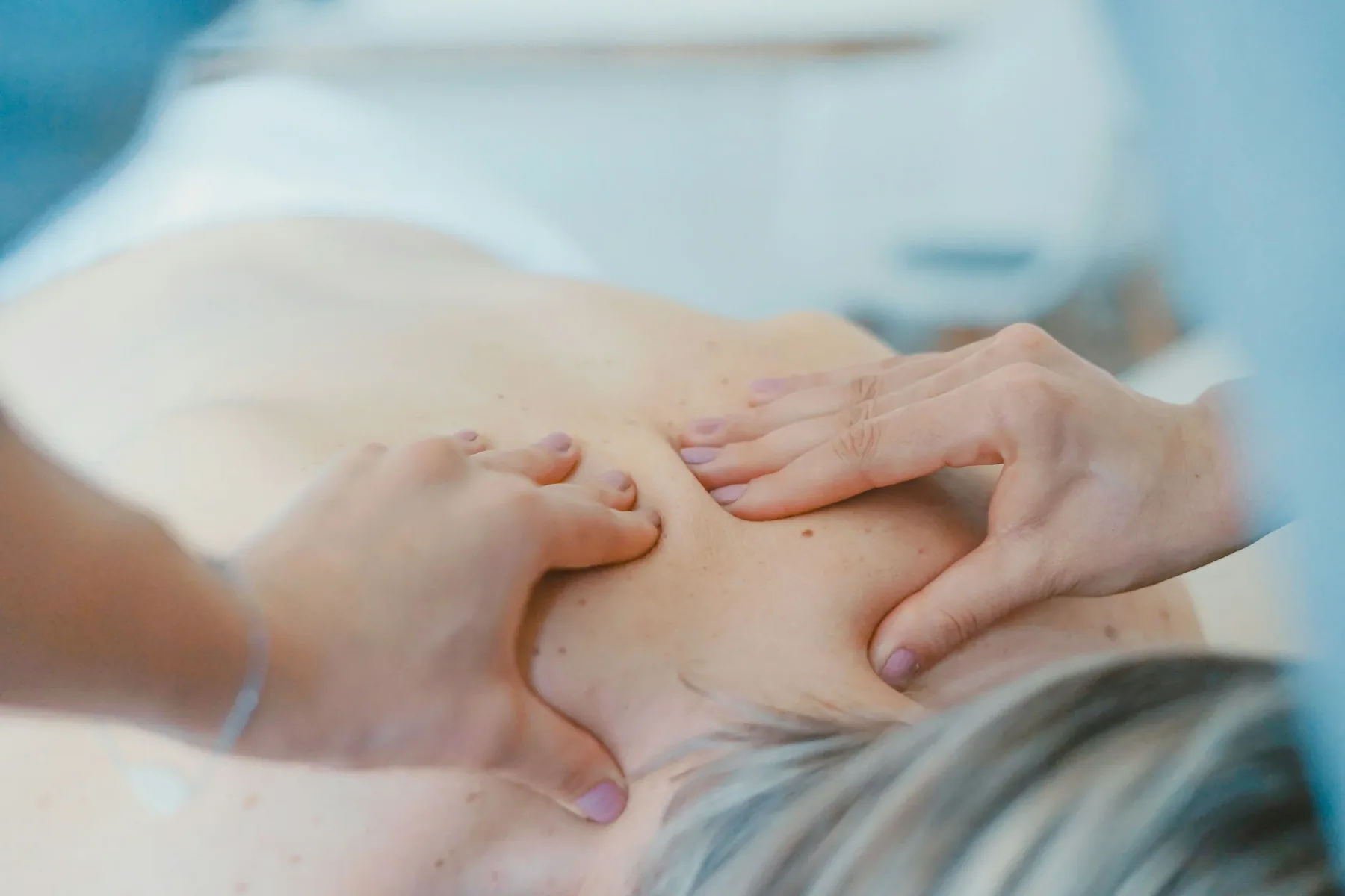 Une personne reçoit un massage des épaules et du cou dans un contexte médical ou de bien-être.